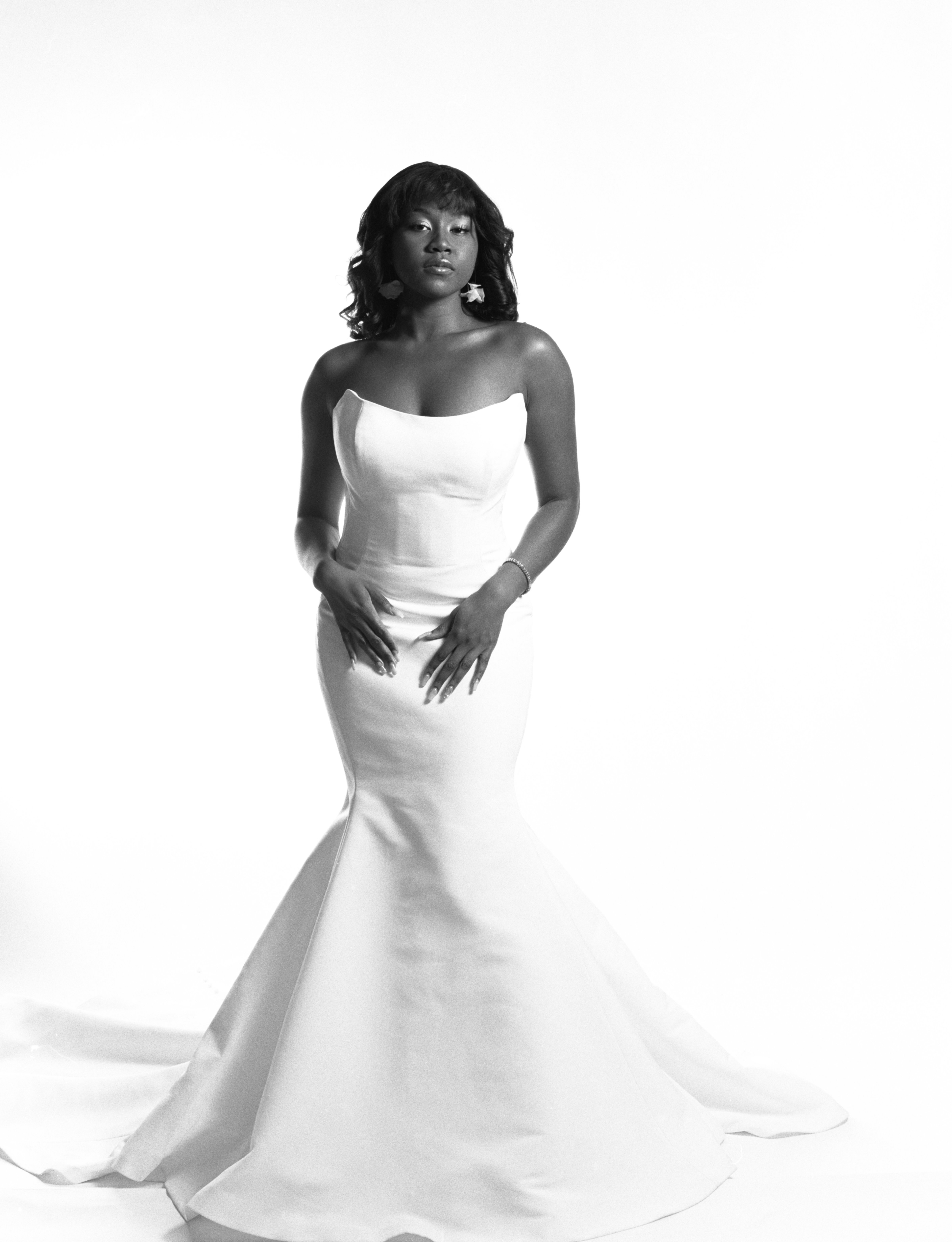 Dramatic black and white photo. Oriana, a tall black woman wearing her hair straightened with bangs, poses dramatically in a strapless ivory wedding gown.