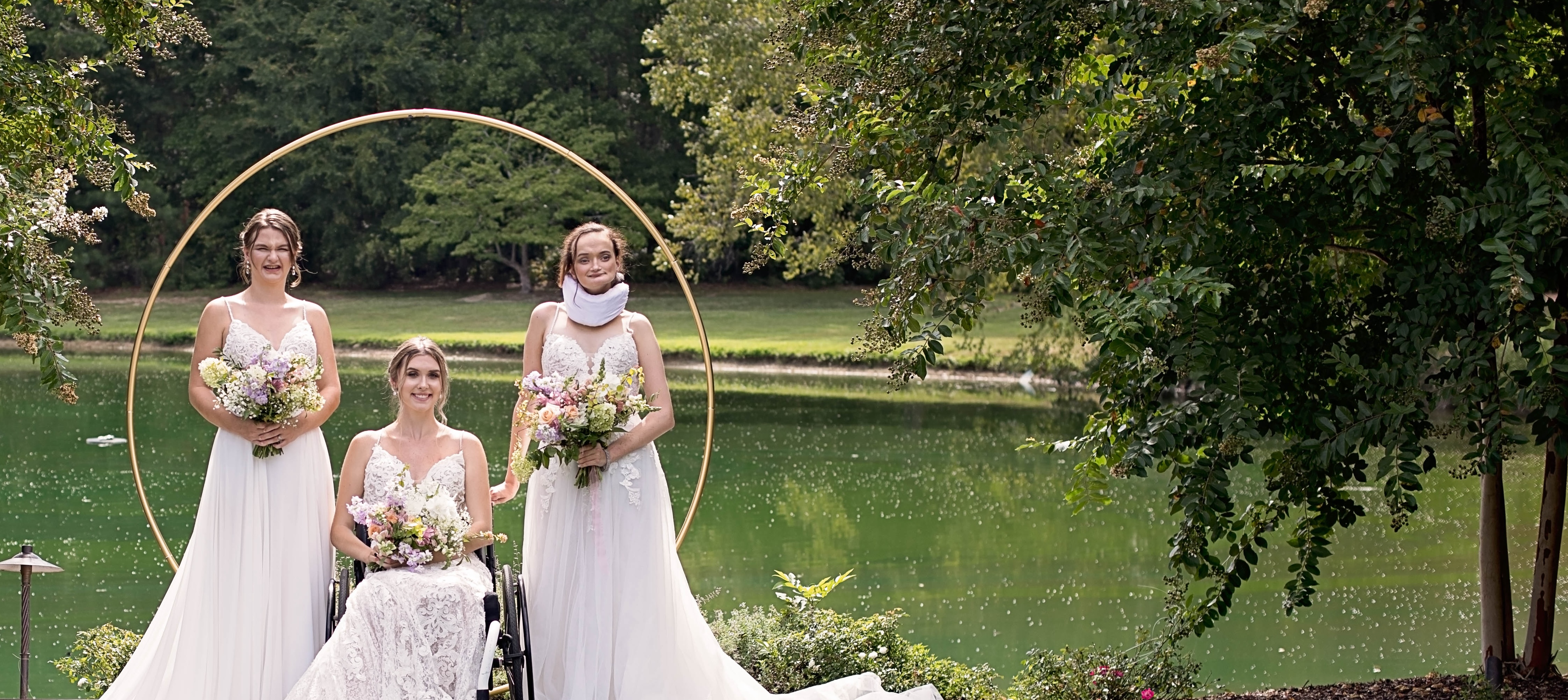 Three white women pose in wedding dresses in front of a gold hoop. Text in a pink circle overlaid on image reads: "Bridal Photoshoots: We are proud to share a glimpse of beautiful images from our previous photoshoots, and hope you love them as much as we do! In collaboration with our sponsors and vendors, these events highlight disabled beauty and joy in bridal."